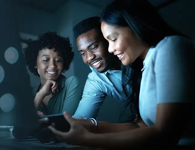 Three people smiling while looking at mobile phone