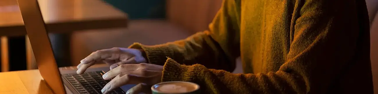 Woman typing on laptop in a cafe with coffee to her left