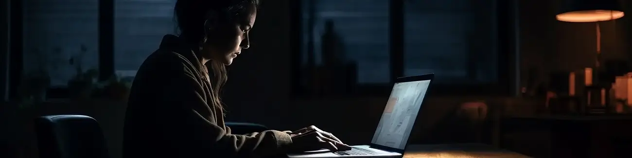 Woman looking down at laptop while typing in dark room