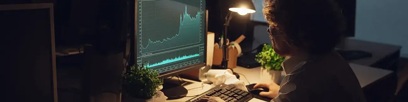 Man looking at computer monitor in a dark room with desk light on