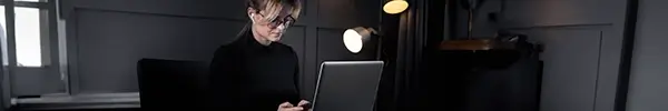 Woman with glasses on and earphones in typing on mobile phone with laptop in front