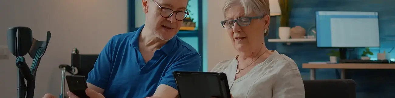 Older man with glasses holding mobile phone while looking at woman with glasses holding tablet