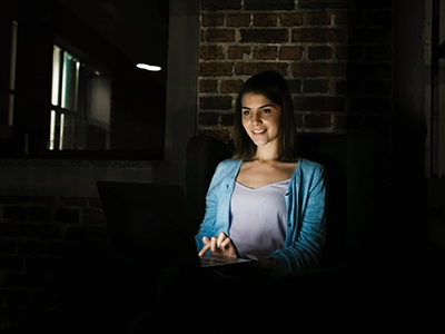 Woman smiling while looking at laptop in dark room