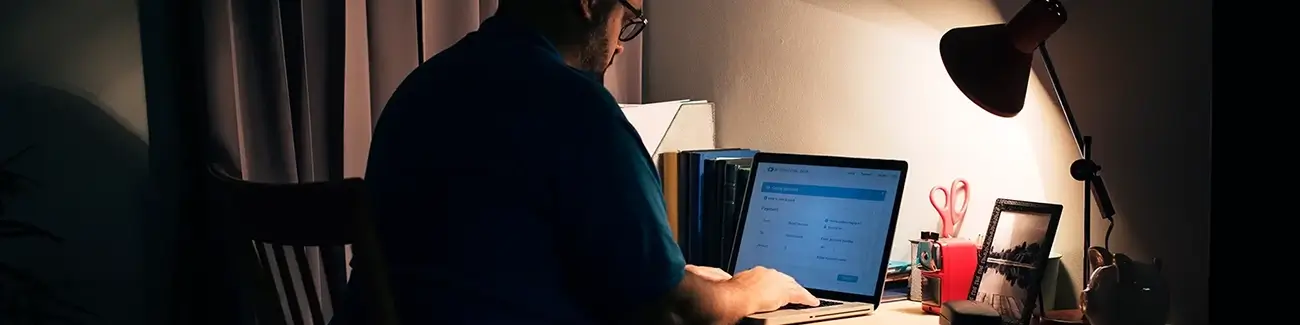 Man with glasses typing on laptop with light shining down