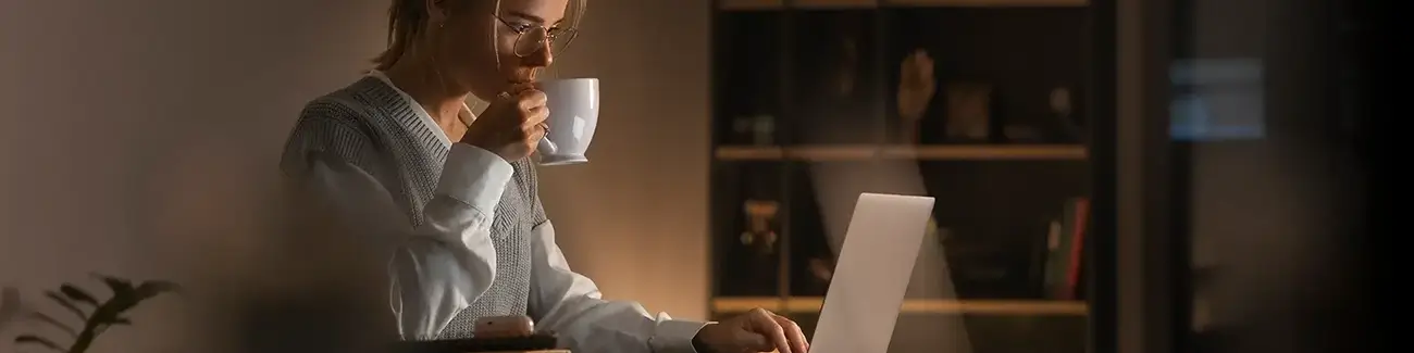 Woman with glasses holding coffee mug with right hand and typing with left