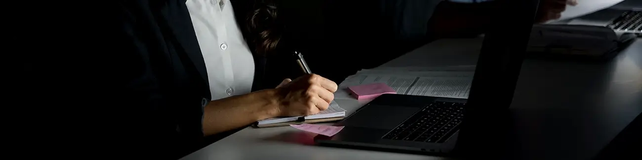 Cyber expert writing notes while looking at laptop