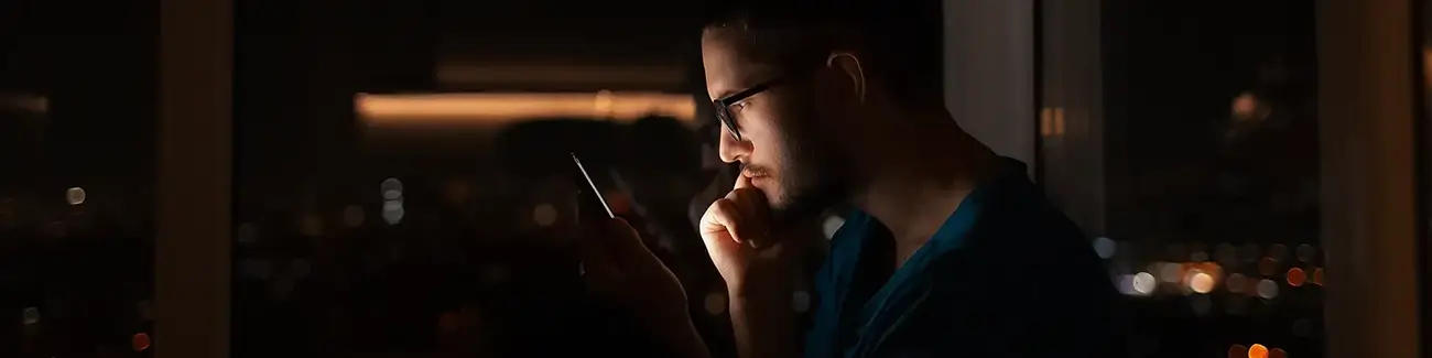 Man with glasses looking worried while looking closely at mobile phone