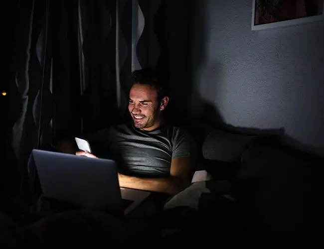 Man smiling while looking at mobile phone in dark